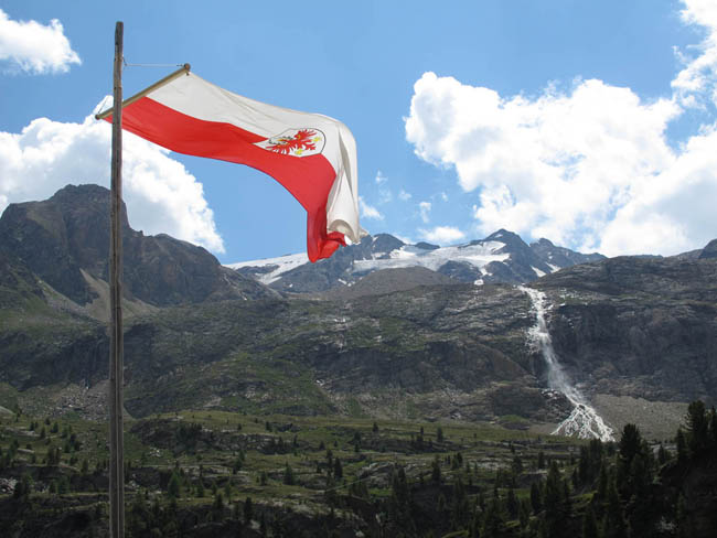 Südtiroler Flagge. Im Hintergrund der imposante Wasserfall, gespeist vom Schranferner zwischen Gipfeln des Punta Martello und der Venziaspitze dahinter.